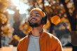 A stylish man with a warm smile and a full beard enjoys the outdoors while listening to music through his vibrant orange and yellow headphones