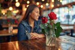 A woman's serene presence complements the vibrant red roses in a glass vase on a wooden table, creating a stunning floral centerpiece that brings the beauty of the outdoors inside