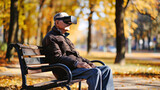 Fototapeta  - An elderly man sits on a bench wearing VR headset glasses, virtual reality. A man with Parkinson's disease walking in city park