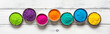 Colored Holi powder in bowls in a row on a white wooden table. Top view, banner. Traditional festival of colors in India.
