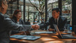 © MP Studio - Two professionals are shaking hands across a table in a bright office setting, smiling in agreement or greeting.