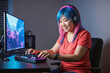 Portrait of young japanese smiling woman with headphones trying a brand new gaming controller on her gamer computer setup with RGB lights at home, professional streamer, copy space for text