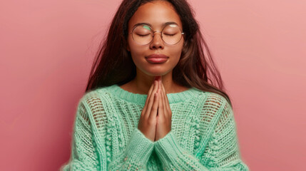 Sticker - A serene woman with closed eyes and hands together in a prayer gesture, wearing round glasses and a soft mint sweater, embodies a moment of peaceful meditation.