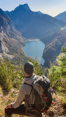 Wall Mural - Hiker man with panoramic view of alpine lake Leopoldsteinersee in Eisenerz, Styria, Austria. Looking at majestic mountain peaks Eisenerzer Alps. Wanderlust in remote Austrian Alps. Mount Pfaffenstein