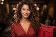 © Alejandra - Retrato de hermosa mujer joven sonriendo con pelo largo castaño sosteniendo una caja de regalo roja. De fondo con efecto bokeh el entorno de una celebracion