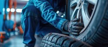 A car mechanic at the service station tries to inflate the tires on the car with the help of a compressor A man in a blue work suit crouched next to a car in a workshop and works around car tir