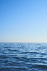 Blue water from the sea with a blue sky. Light comes from the right. Vertical format, also suitable as a poster or background. Free space for text, objects or other things.