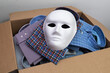 A white mask lies on shirts in an open cardboard box, a concept on the theme of counterfeit products and smuggling
