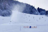 Fototapeta Tulipany - Snow gun making snow in Kranjska Gora, Slovenia, with skiers in the background on the slopes