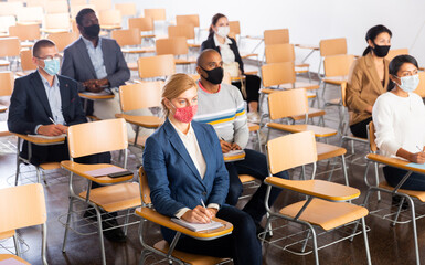 Wall Mural - Group of diverse business people wearing face masks for viral protection and keeping social distance listening to speaker at conference, the new normal