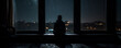 Alone, a man sits by a window veiled by the night's rain, distant city lights punctuating the darkness. conveys a poignant blend of reflection and stark isolation felt even within the urban sprawl.