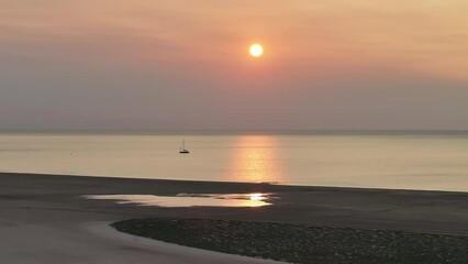 Wall Mural - A sailboat anchored in a peaceful bay, bathed in the sunlight of a soft sunrise with gentle reflections on the water - drone moves forward slowly