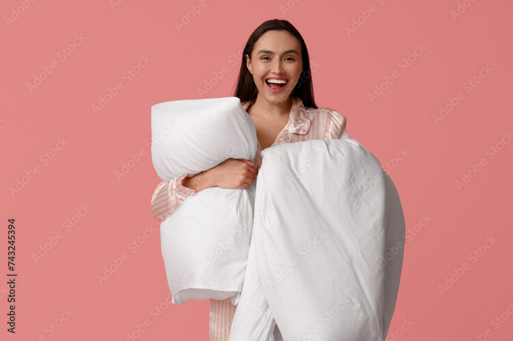 Pretty young woman with blanket and pillow on pink background