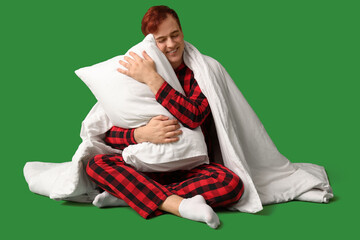 Wall Mural - Handsome young happy man with blanket and pillow sitting on green background