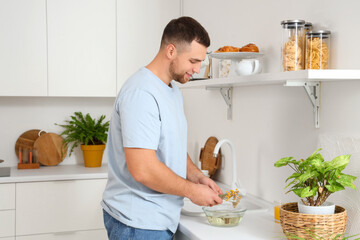 Wall Mural - Young man preparing steam inhalation with herbs at table in kitchen