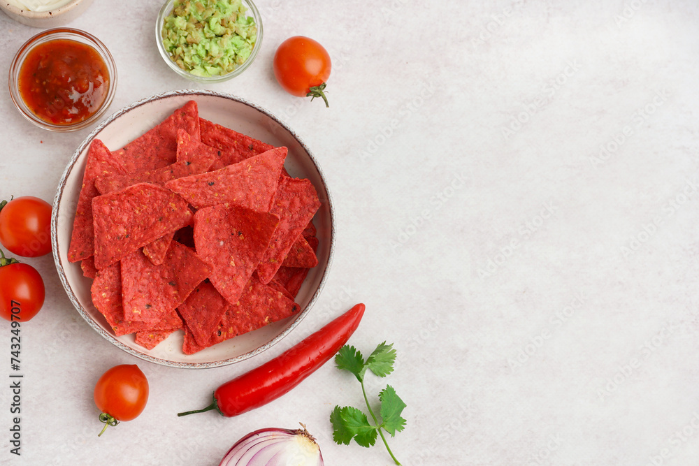 Bowl with red nachos, vegetables and sauces on white grunge background