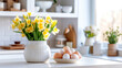 Easter table setting with yellow flowers in a vase and colored Easter eggs in the white Scandinavian-style kitchen background. Beautiful minimalist design for greeting card