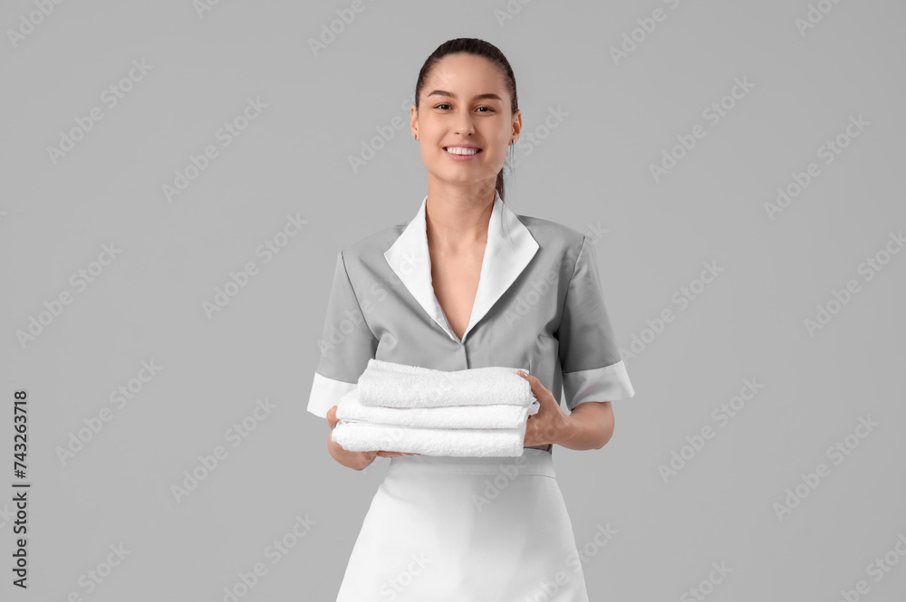 Young chambermaid with clean towels on light background