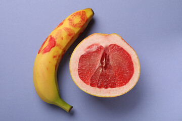 Wall Mural - Banana with red lipstick marks and half of grapefruit on violet background, flat lay. Sex concept