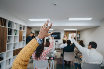 Wall Mural - Focused group of people in a workshop setting with raised hands eager to ask questions or provide answers during an interactive session.