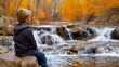 © weerasak - A boy sitting on a rock by a river, surrounded by autumn leaves and flowing water