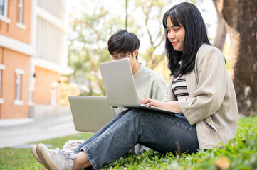 Wall Mural - Two young Asian college students are discussing work and using their laptop at a campus park.