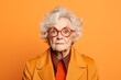 Funny senior woman in orange coat and red glasses on orange background