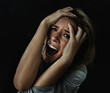 © Jeff Bergen/peopleimages.com - Portrait, horror and fear with woman screaming in studio on black background for reaction to danger. Face, stress and mental health with scared young person in dark for phobia, nightmare or terror