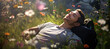 A happy man lying on his back on the green grass among many flowers in a meadow. Blissful relaxation time outside in the nature.
