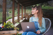 © olezzo - Young happy woman in denim overalls sitting with a laptop on the terrace of a country house on a spring day