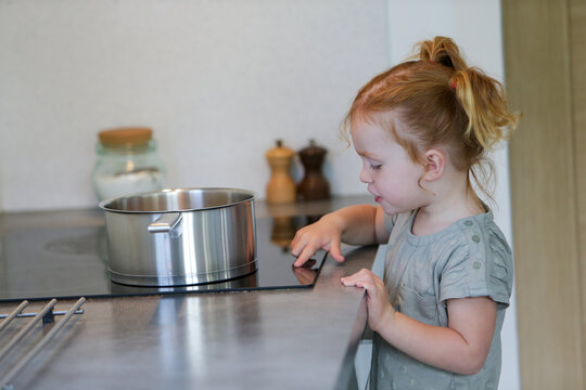Little girl in a kitchen with a metal pan touching the hob knobs

