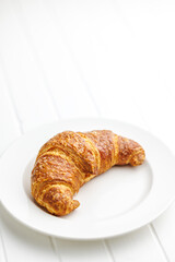 Wall Mural - Baked tasty croissant on plate on white table.