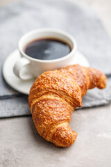 Poster - Baked tasty croissant and coffee cup on kitchen table.