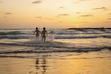 Poster - Happy teenager boys, running and playing on the beach on sunset, splashing water and jumping on the sand