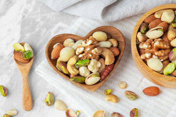 Wall Mural - Nuts mixed in heart wooden bowl on marble table with linen cloth