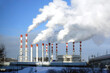 Thermoelectric power station building with many high red and white industrial pipes with dense smoke under winter sky on sunny day front view