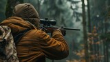 Fototapeta Sport - Hunter during hunting in forest. Hunter holding a rifle and aiming at deer. hunting expedition in the forest wearing brown jackets and reflective gear