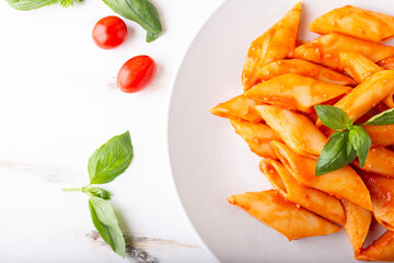 Wall Mural - Pasta with fresh tomatoes sauce and basil. Penne with tomatoes served on a white background. Italian typical dish.