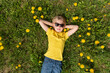 © somemeans - Happy boy puts his hands behind his head. Blond child lies on grass in dandelions field and dreaming. Top view