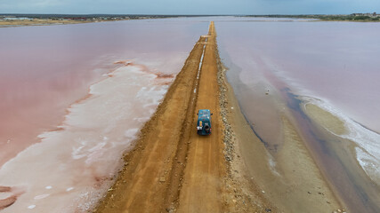 Poster - A green camper on a dirt track between pink and brown salt flats