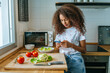 Woman in the kitchen with mobile phone, while preparing salad.