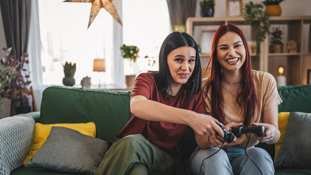 Two young women caucasian friends or sisters play console video game