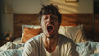Man yawning or orgasm while sitting on a bed with morning sunlight filtering through the room.