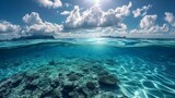 Fototapeta Do akwarium - Above and below the surface of the sea with a coral reef underwater and a cloudy blue sky.