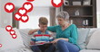 Image of heart icons over caucasian grandmother and grandson reading book in livin groom