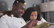 Image of roses over happy african american father and daughter reading book