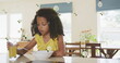 Image of roses over african american girl drinking juice and eating breakfast