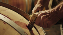 A Closeup Of A Winemakers Hands Expertly Hammering A Bung Into A Barrel Sealing In The Wine And Locking It Away Until It Is Ready To Be Enjoyed. The Smell Of Yeast And Fermentation