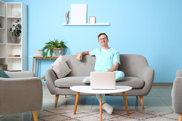 Wall Mural - Redhead young male doctor with laptop sitting on sofa at home