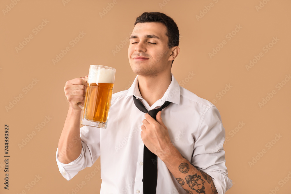 Handsome young happy man with mug of beer on brown background